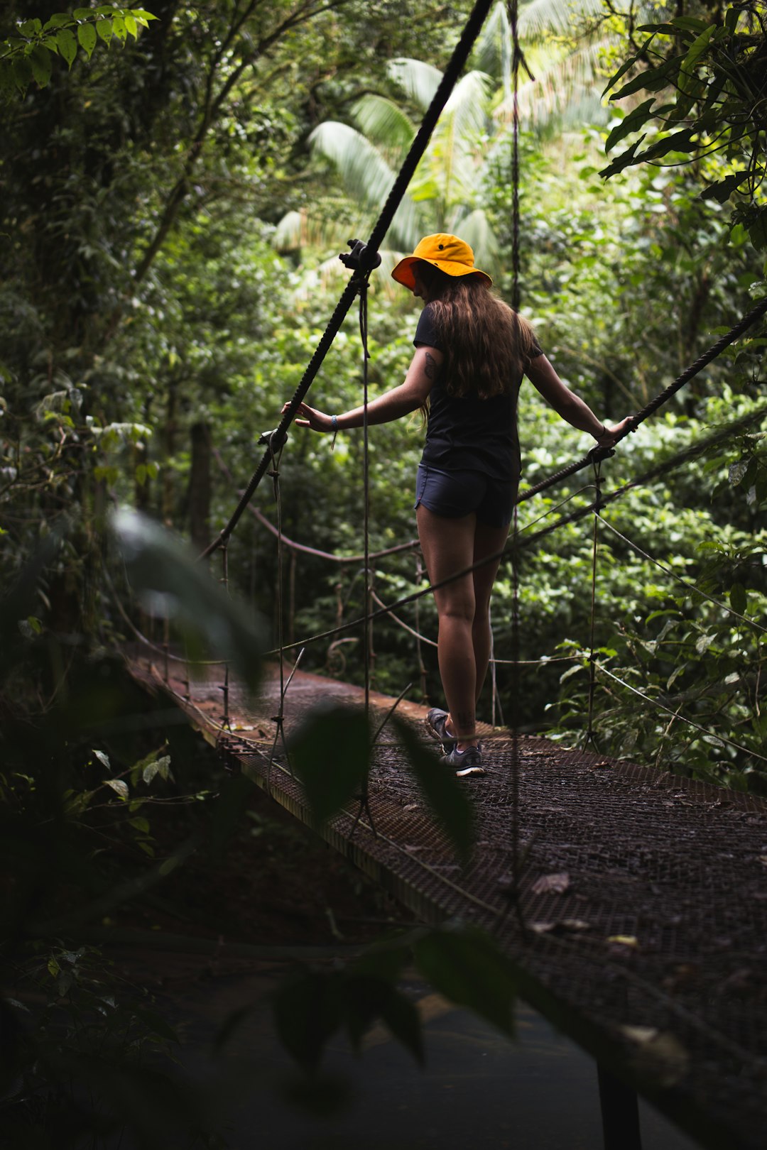 woman in black t-shirt and blue denim shorts walking on hanging bridge