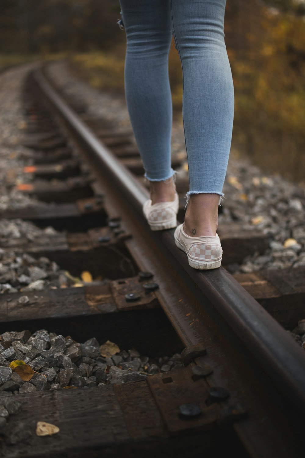 person in blue denim jeans and white low top sneakers standing on train rail during daytime
