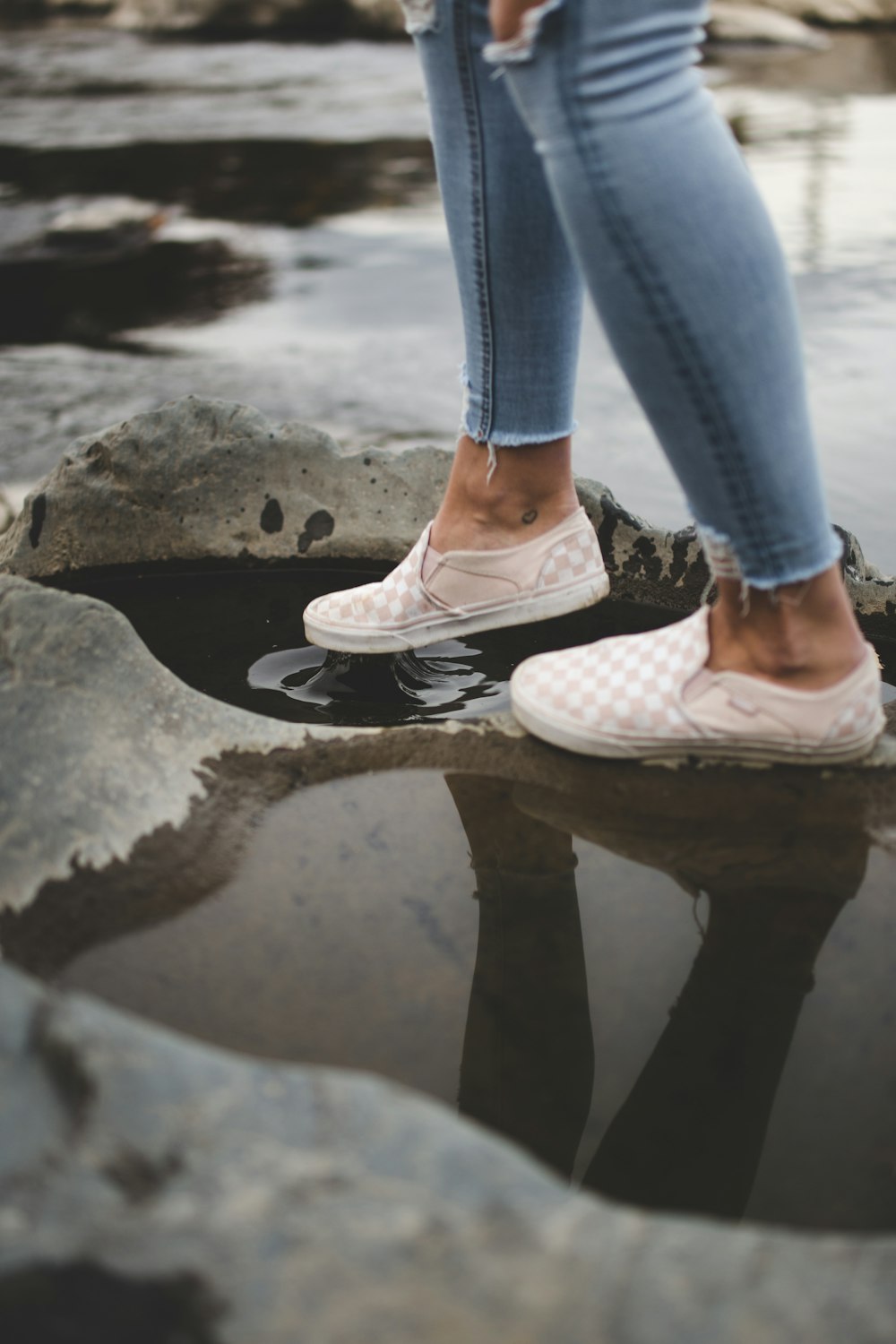 Person in blauen Jeans und weißen Turnschuhen auf grauem Betonpflaster