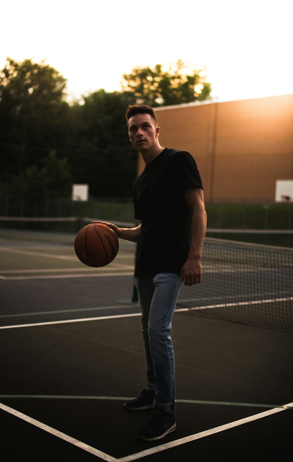 黒のクルーネックTシャツとブルーデニムジーンズを着た男が昼間にバスケットボールをしている