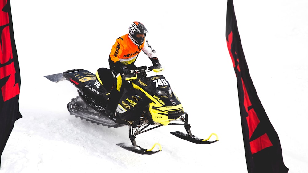 hombre con traje de nieve rojo y negro montando moto de nieve negra y amarilla