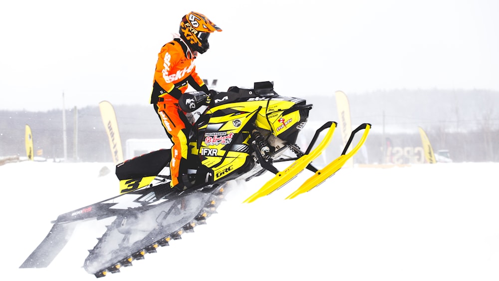 man in orange jacket riding yellow snow mobile