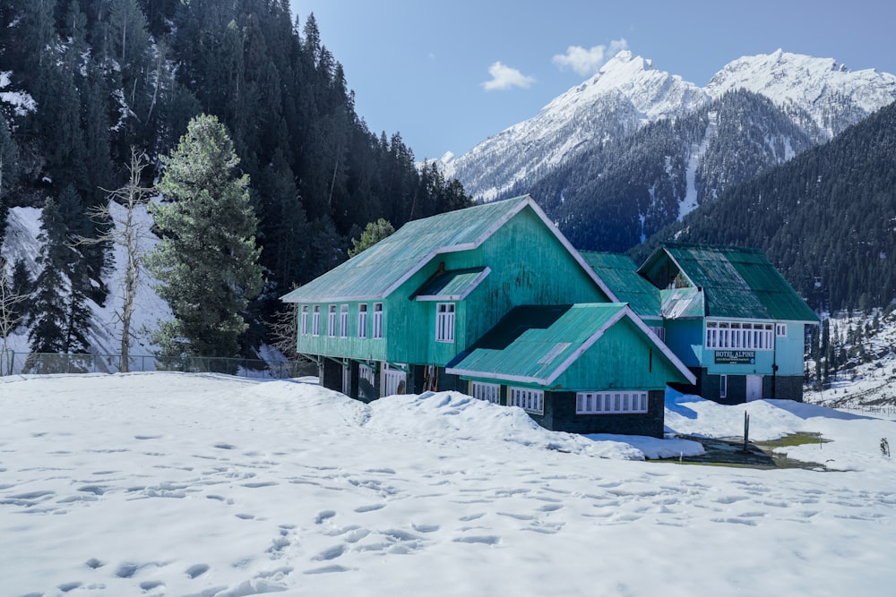 casa de madeira verde no chão coberto de neve perto de árvores verdes e montanha durante o dia