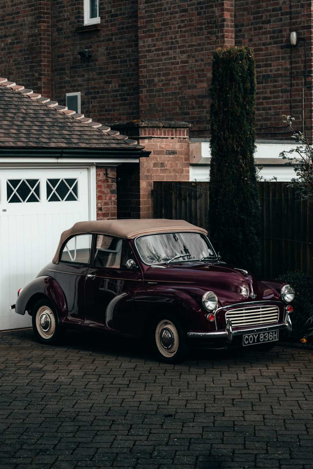 red classic car parked beside brown brick house