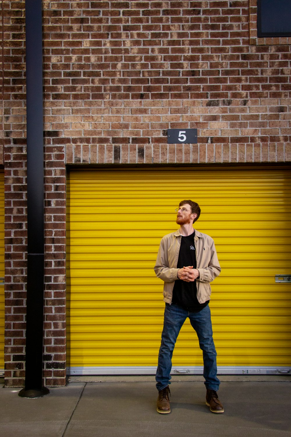 uomo in camicia bianca e jeans blu in denim in piedi accanto al muro di mattoni marrone