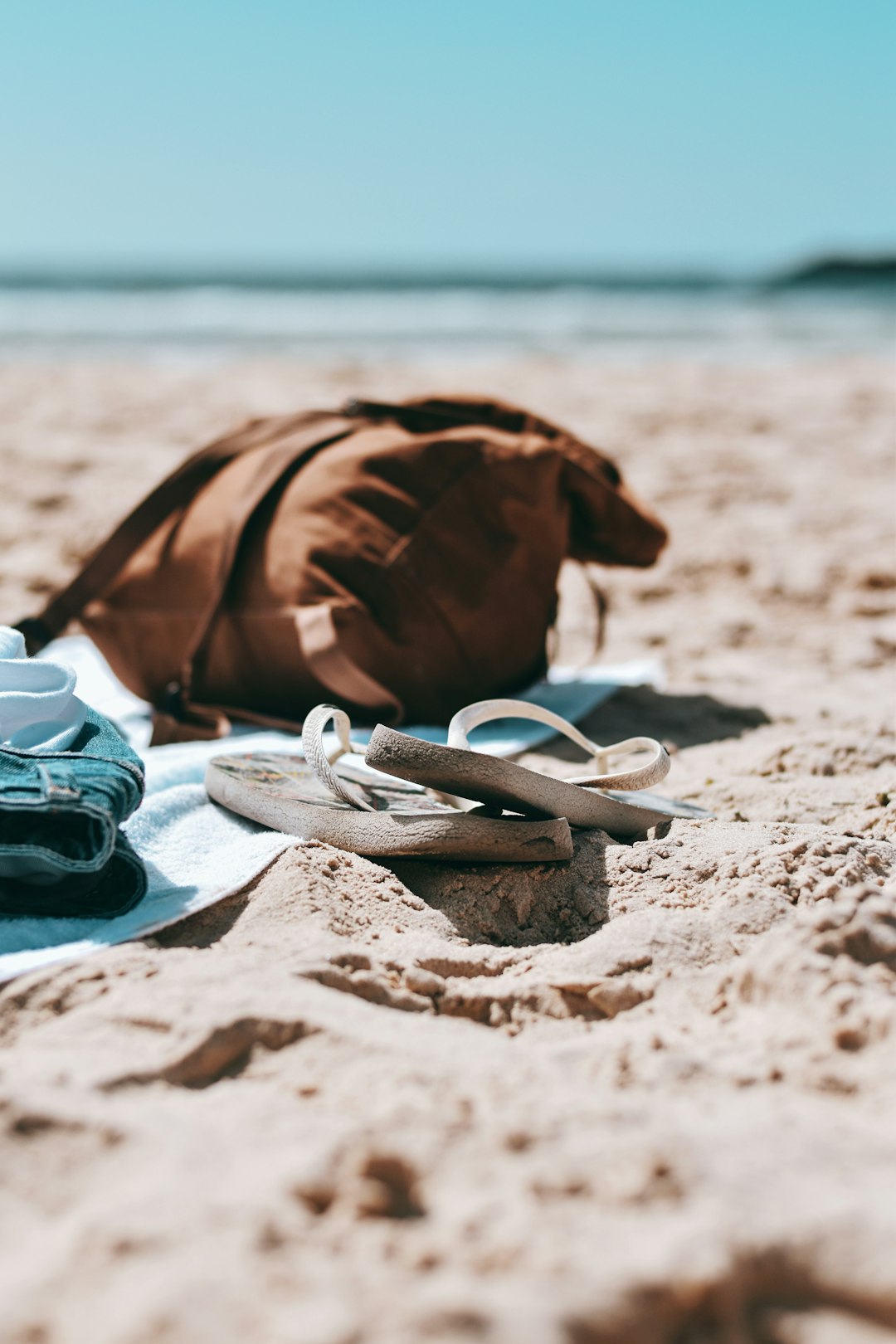 white flip flops on brown sand near black and white sneakers