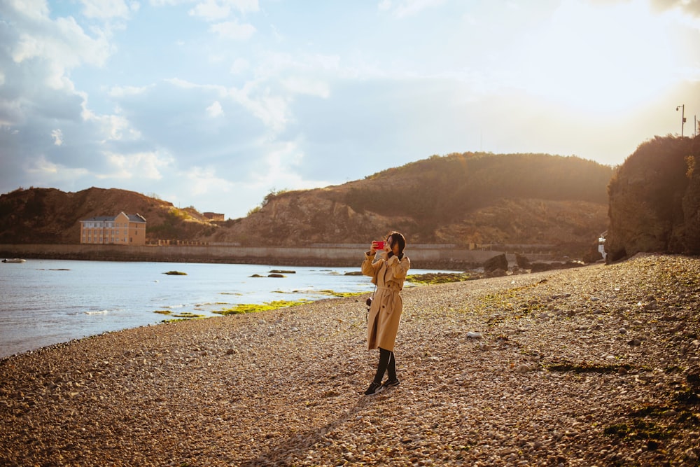 woman in brown coat standing on brown sand near body of water during daytime