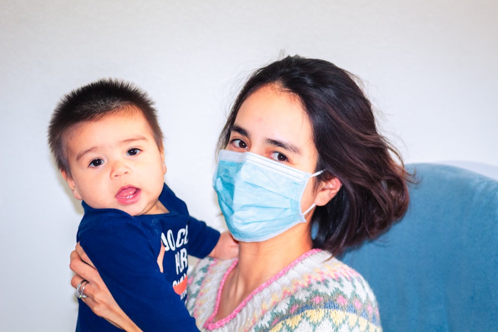 woman in blue shirt carrying baby in blue and white hoodie