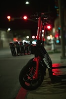 A shiny Royal Electra electric scooter parked on a city street at dusk with glowing neon lights.