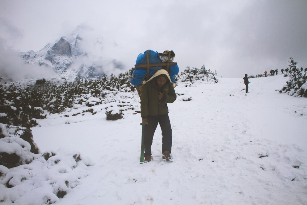 man in brown jacket and black pants with blue backpack standing on snow covered ground