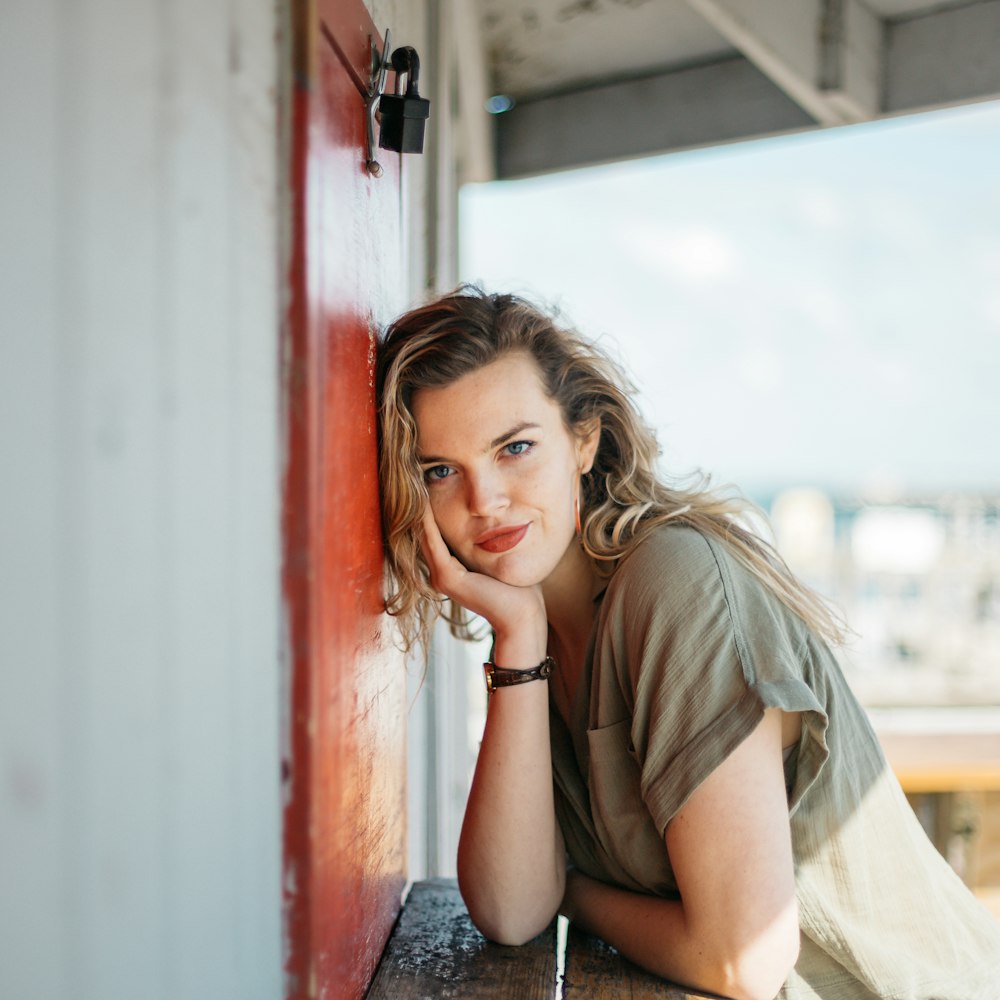 woman in brown t-shirt and blue denim jeans sitting on red wooden wall