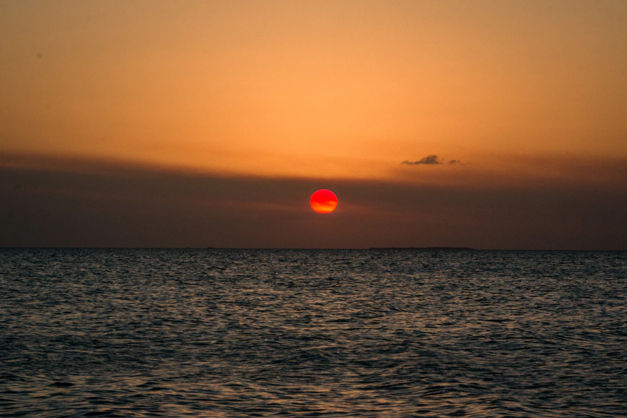 A red sun sinking into a flat, calm sea under an orange evening sky.