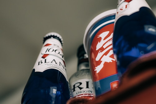 Several beverage containers with diverse labels and designs are arranged, featuring blue and red colors prominently. One bottle has 'Blanc 1664' written on it, and others include a mix of text and abstract designs.