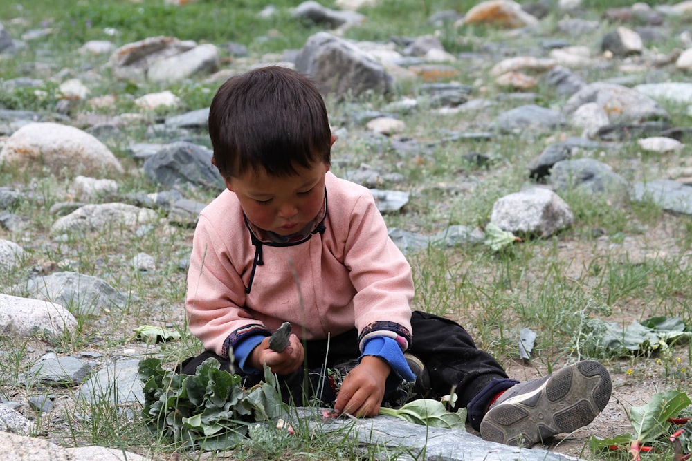 boy in brown jacket sitting on green grass during daytime