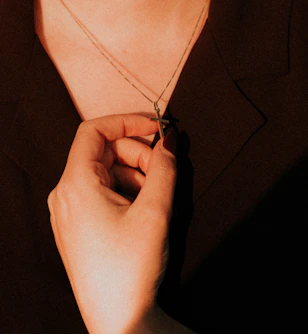 Close-up of hands holding a handcrafted wooden cross necklace glowing softly in natural light.