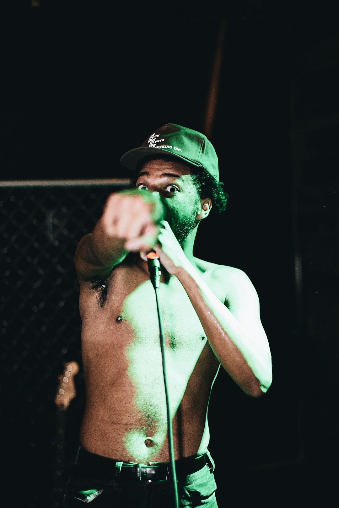 topless man wearing black cap holding microphone