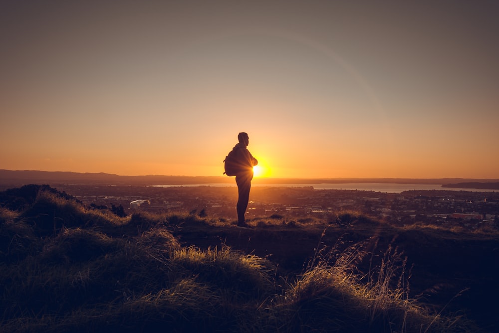 silhouette of man standing on grass field during sunset