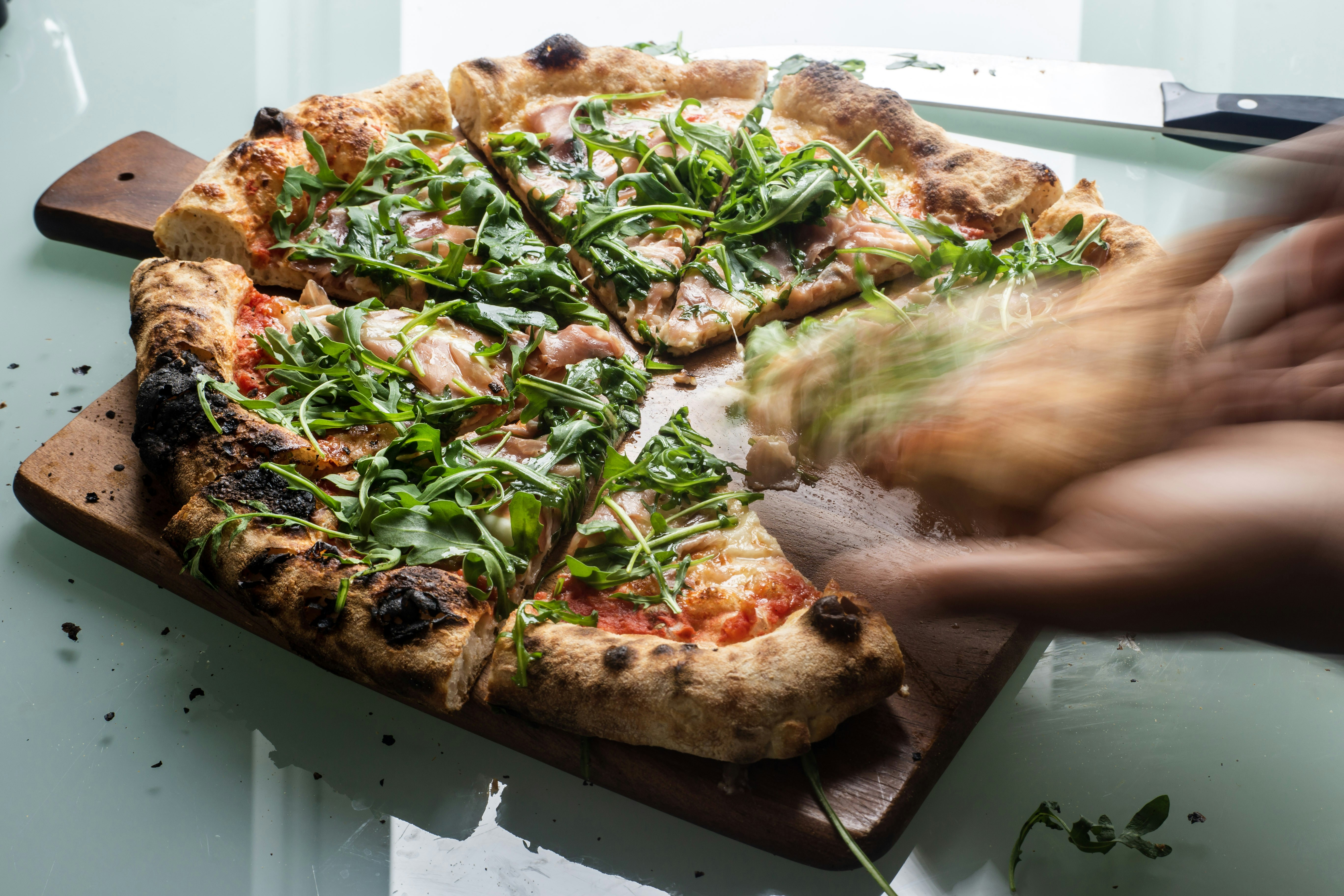 Hand reaching for pizza topped with rocket