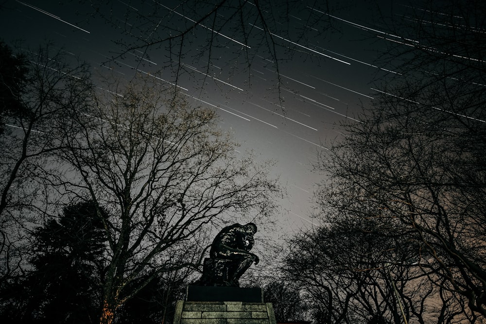 black statue of man sitting on rock under blue sky during daytime