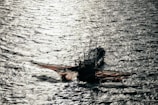 A fishing boat with large nets cast out on the sides floats on the water, with shimmering sunlight reflecting off the rippling surface of the sea.