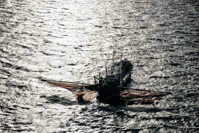 A fishing boat with large nets cast out on the sides floats on the water, with shimmering sunlight reflecting off the rippling surface of the sea.