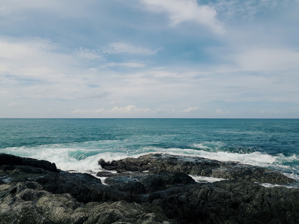 ocean waves crashing on rocky shore under white clouds and blue sky during daytime