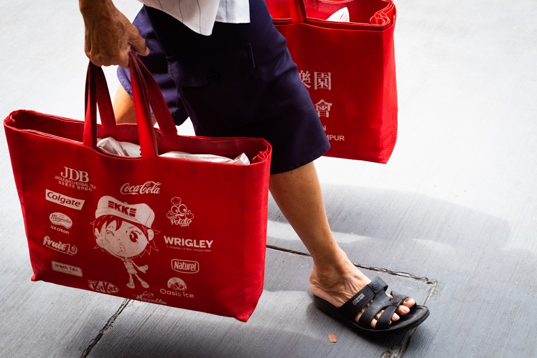 person in black shorts and black sandals holding red tote bag