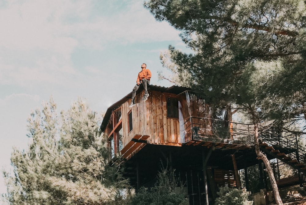 man in black leather jacket standing beside brown wooden house during daytime