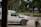 A white Land Cruiser with the World Vision logo is parked on a dirt road. A red motorcycle is nearby, with tropical trees and a simple building in the background, suggesting a rural setting.