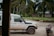 A white Land Cruiser with the World Vision logo is parked on a dirt road. A red motorcycle is nearby, with tropical trees and a simple building in the background, suggesting a rural setting.