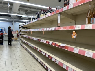 A retail store aisle with empty shelves and a worried store owner observing the surroundings.