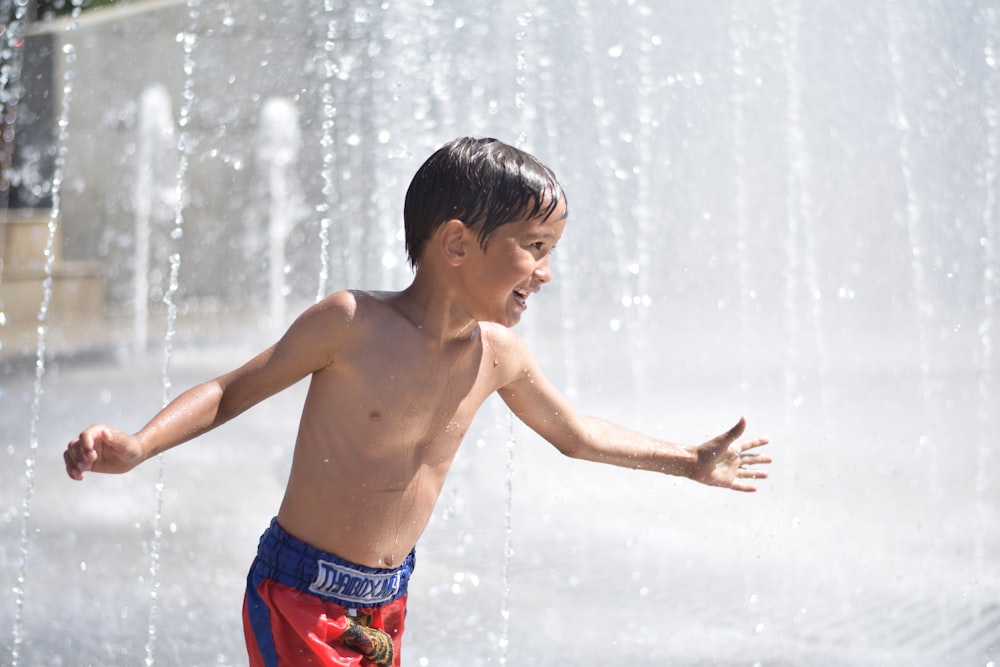 boy in red and blue shorts standing on water fountain during daytime