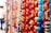A vibrant collection of colorful beads is strung together in various strands. The beads are of different shapes, sizes, and colors, including shades of red, yellow, orange, blue, and green. The background is slightly blurred, giving prominence to the beads in the foreground, with some areas appearing in soft focus.