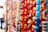 A vibrant collection of colorful beads is strung together in various strands. The beads are of different shapes, sizes, and colors, including shades of red, yellow, orange, blue, and green. The background is slightly blurred, giving prominence to the beads in the foreground, with some areas appearing in soft focus.