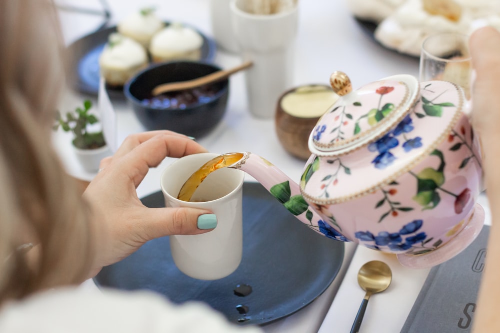 person pouring tea on white ceramic mug