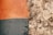 A textured surface showing a contrast between a smooth, painted area on the left and a rough, textured area on the right. The painted section has an orange hue on top and a blue-grey hue beneath, while the textured area appears to be an unpainted, bare section of plaster or concrete with a coarse, uneven finish.