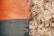 A textured surface showing a contrast between a smooth, painted area on the left and a rough, textured area on the right. The painted section has an orange hue on top and a blue-grey hue beneath, while the textured area appears to be an unpainted, bare section of plaster or concrete with a coarse, uneven finish.