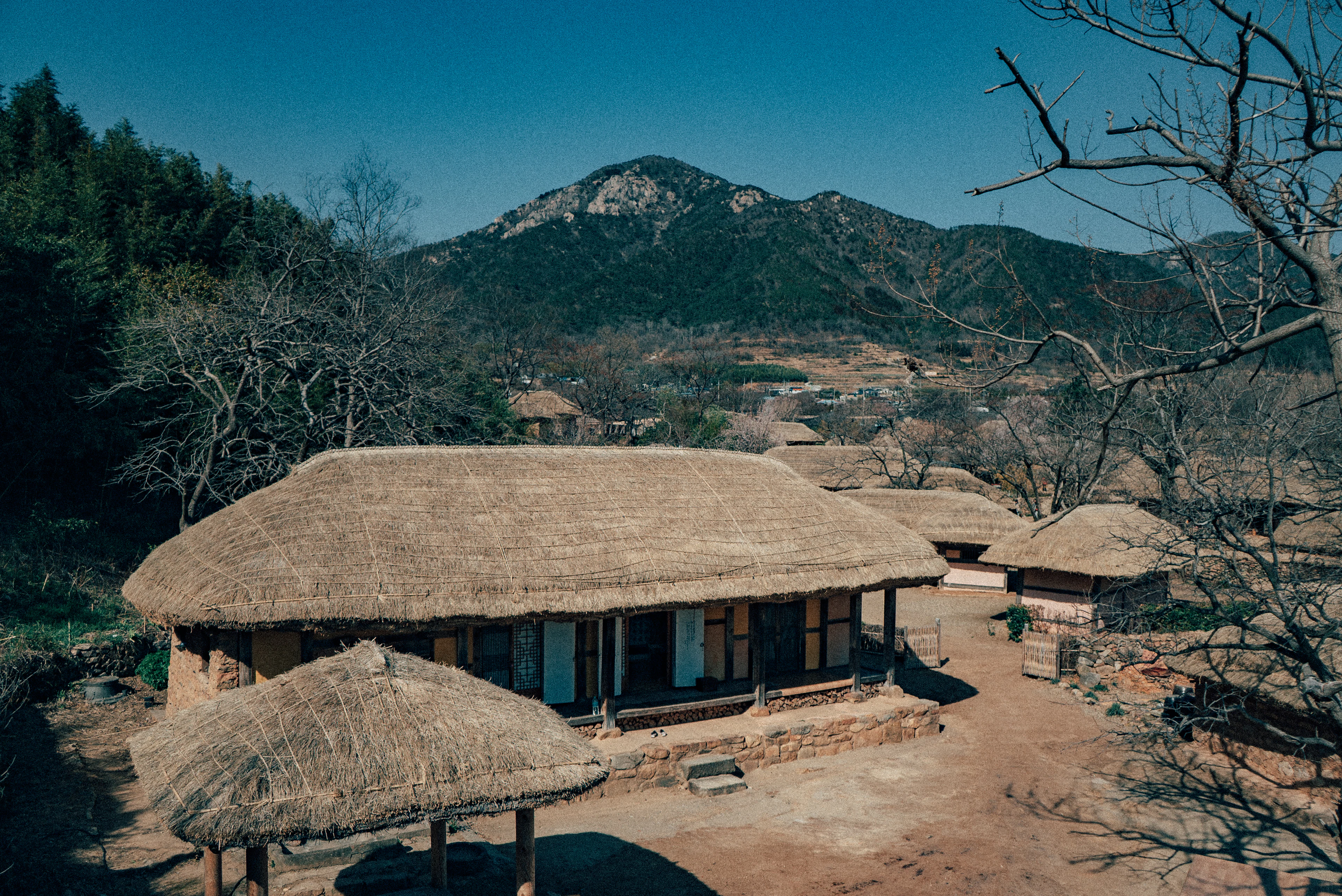 Thatched-roof houses in a Korean folk village beneath a rocky mountain