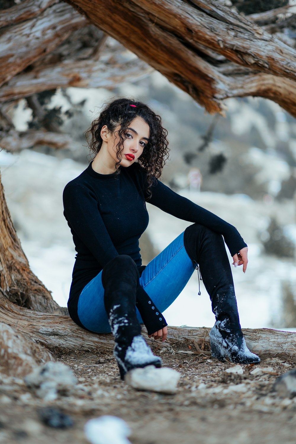 woman in black long sleeve shirt and blue denim jeans sitting on brown tree log during