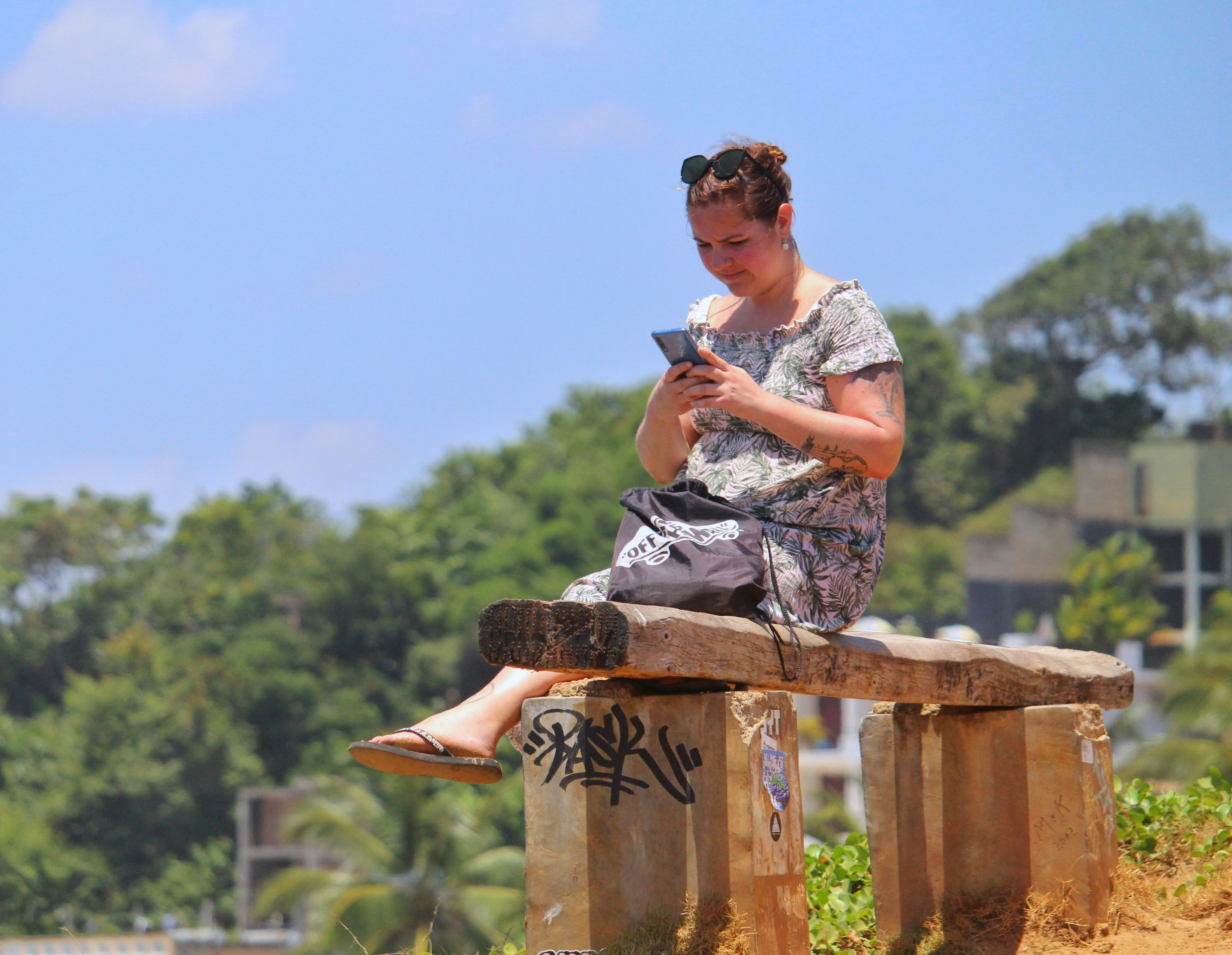 man in white and grey floral shirt sitting on brown wooden fence during daytime
