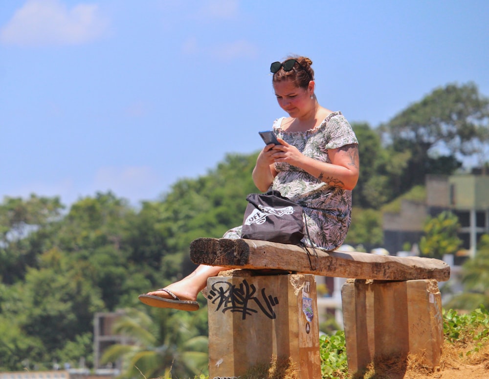 man in white and grey floral shirt sitting on brown wooden fence during daytime