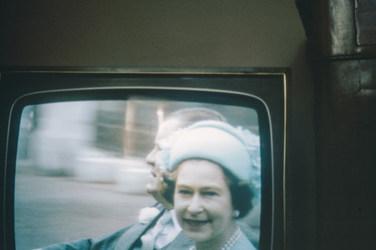 A television screen displays a vintage broadcast, featuring a person in a light blue outfit and hat. The image has a soft, blurry quality typical of older television screens.