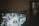A television screen displaying a ceremonial event with two people in formal attire. The image is slightly blurred and appears to be a broadcast of a parade or public celebration.