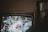 A television screen displaying a ceremonial event with two people in formal attire. The image is slightly blurred and appears to be a broadcast of a parade or public celebration.