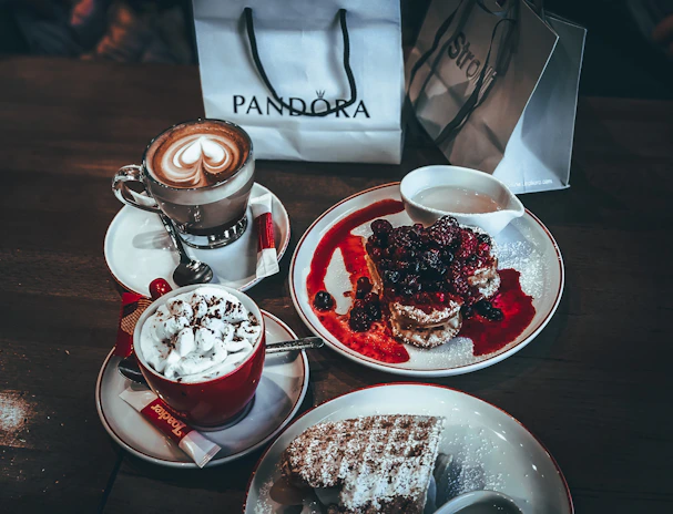 Smiling friends clinking coffee cups over a table filled with customized waffles and toppings inside a cozy restaurant.