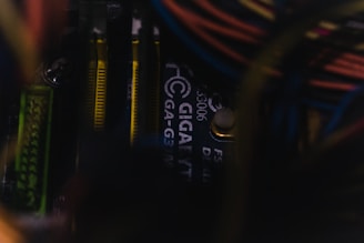 Close-up view of a computer motherboard with visible Gigabyte branding, featuring various components like RAM sticks and wiring. The image is dimly lit, adding a moody and technical ambiance.