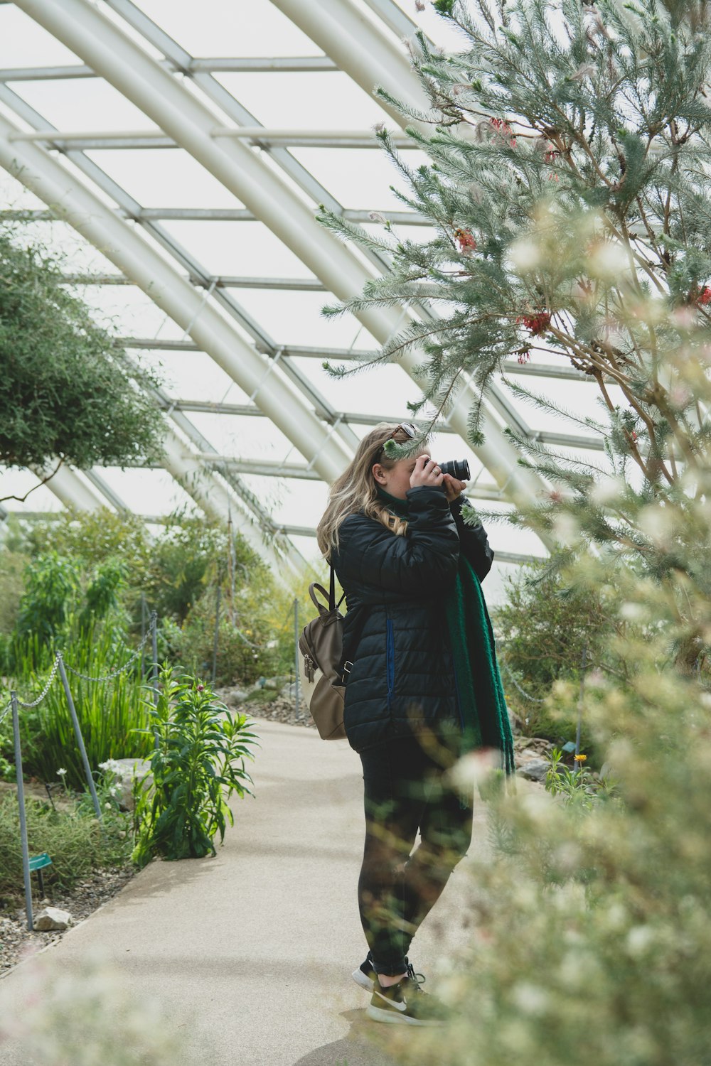 woman in brown jacket standing in the middle of green plants