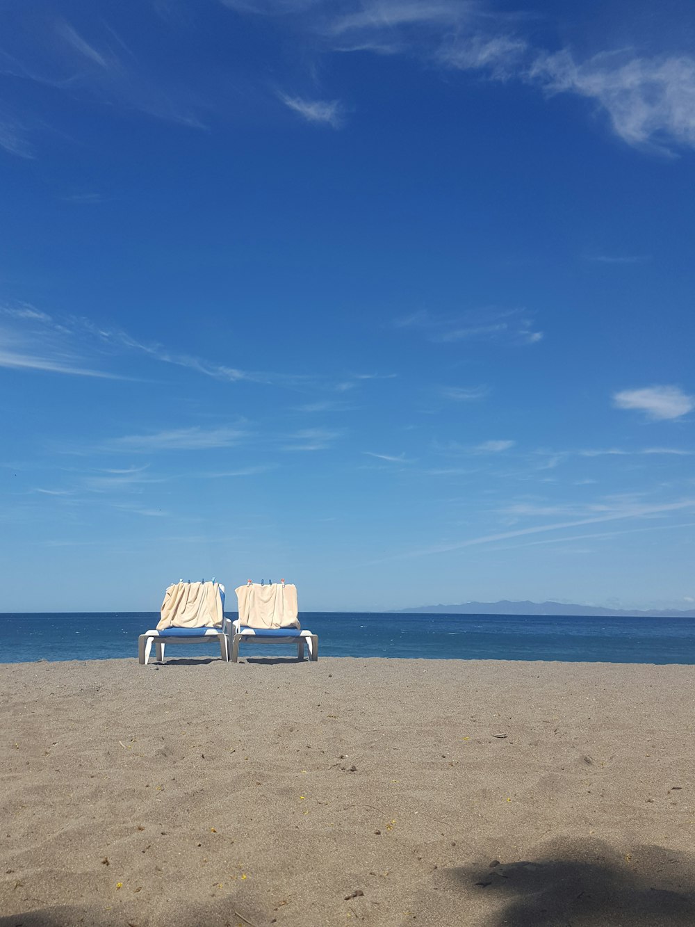 white and blue lounge chairs on brown sand under blue sky during daytime