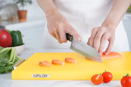A smiling person using a stylish cutting board and knife set while preparing a vibrant salad.