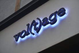 The word 'volt age' is displayed on a wall with bold black letters that are illuminated by a soft blue neon light, casting a glow around the edges.